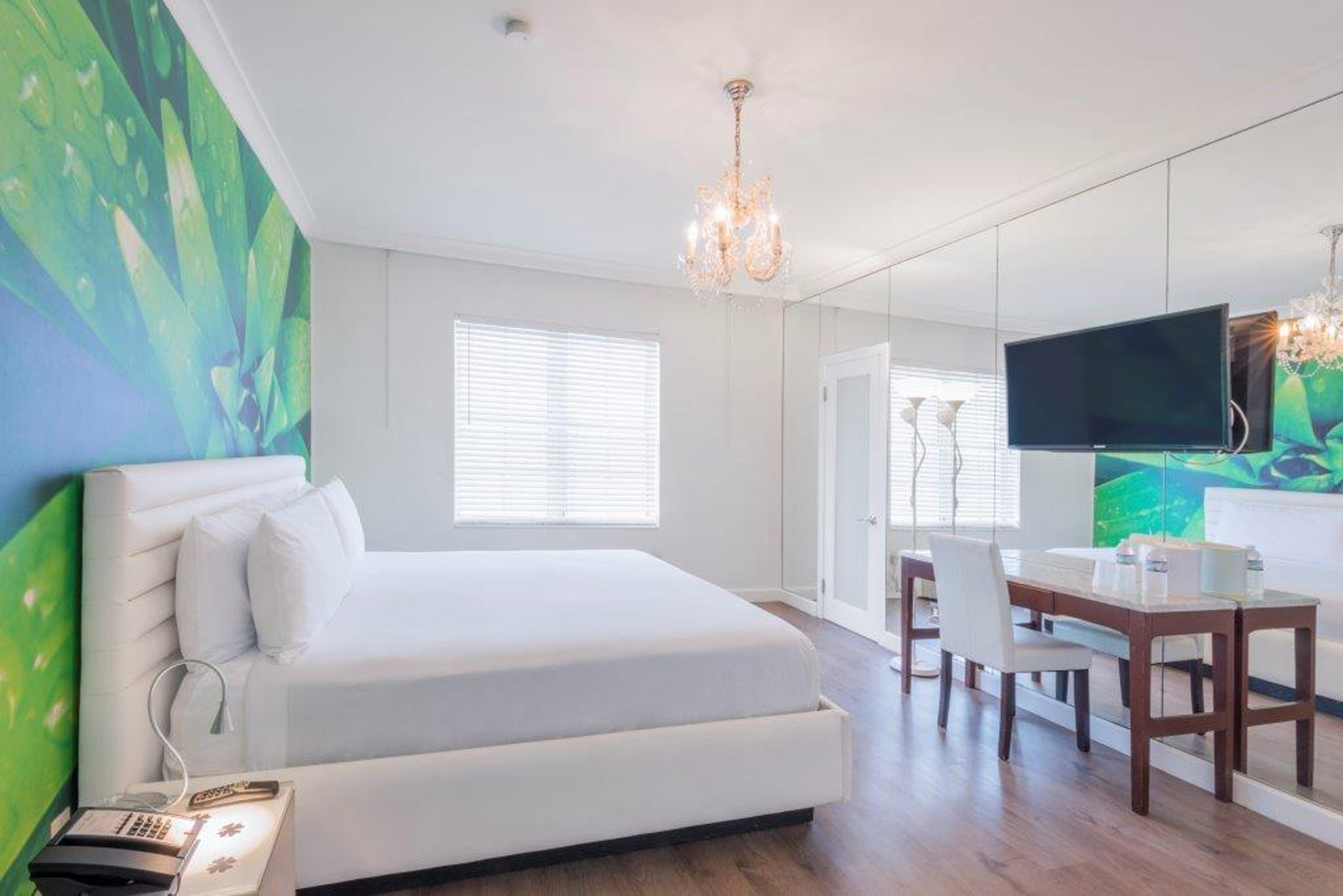 A bright and modern hotel room with a large bed, desk, TV, and chandelier.