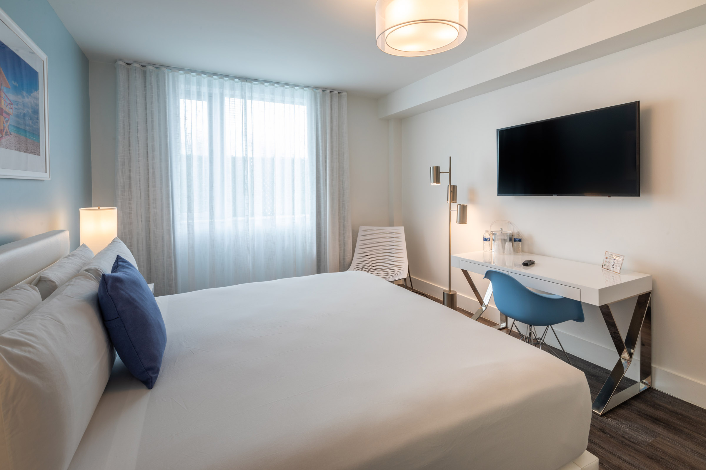 A hotel room with a bed, desk, TV, and window.