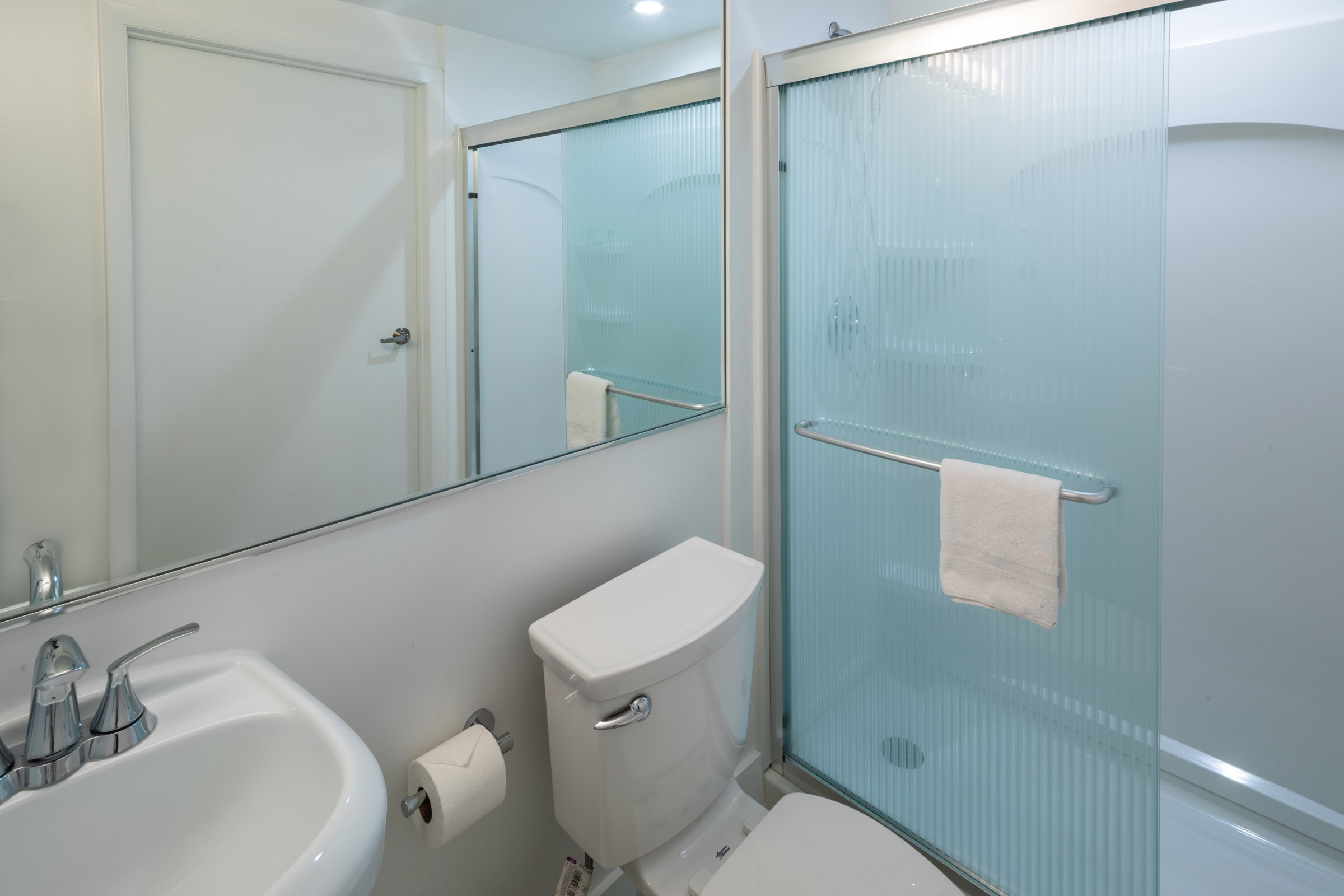 A clean bathroom with a toilet, shower, sink, and mirror.
