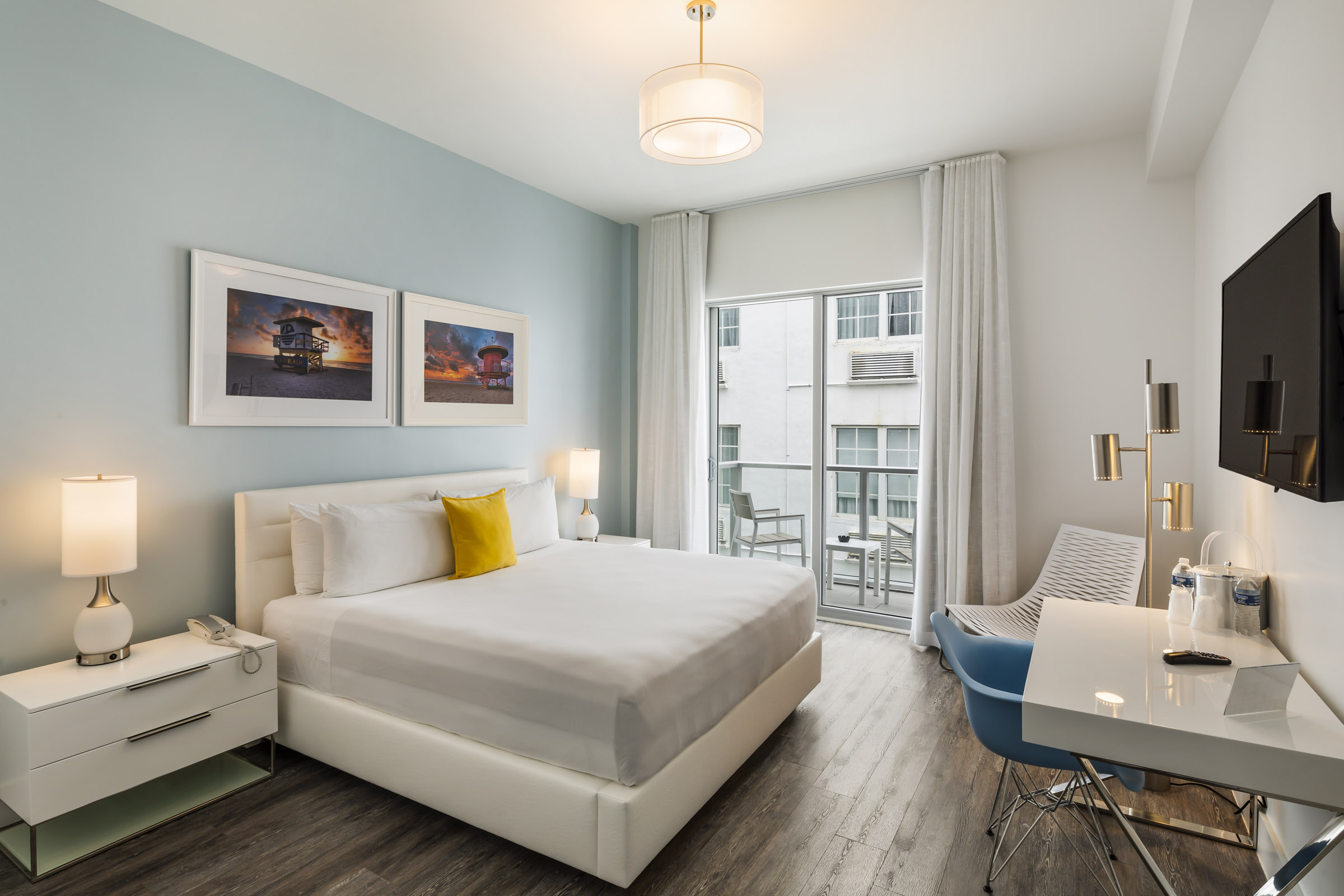 A hotel room with a king-size bed, balcony, flat-screen TV, and desk