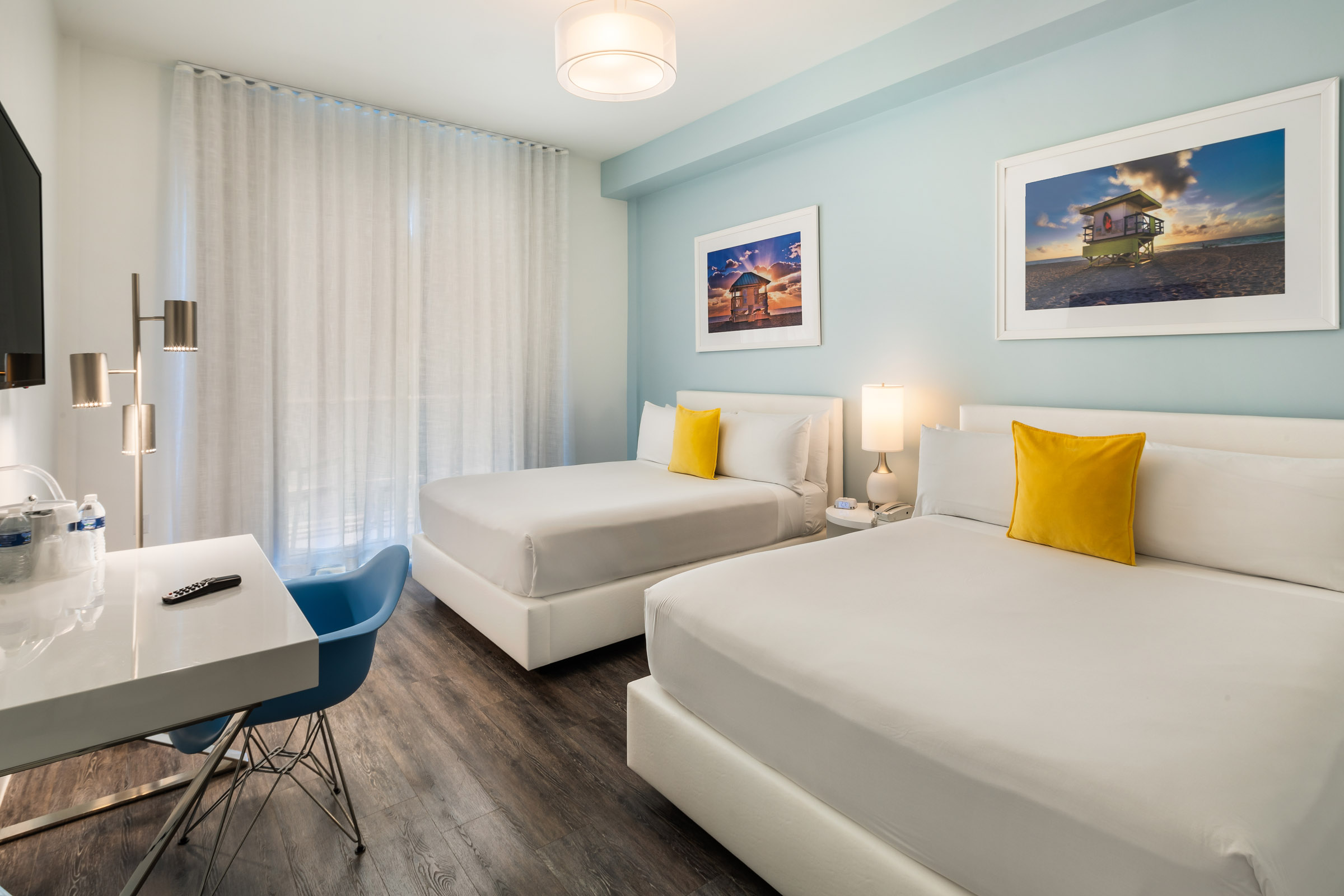 A clean and modern hotel room with two twin beds, a desk, and a chair.
