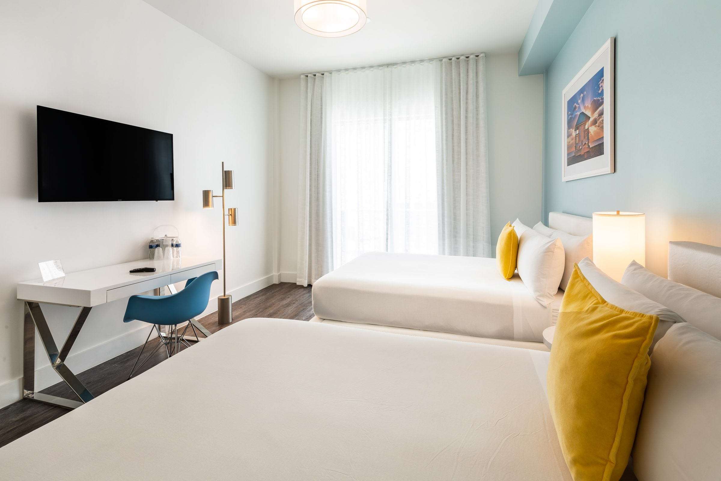 A hotel room with two beds, a desk, and a TV on the wall.