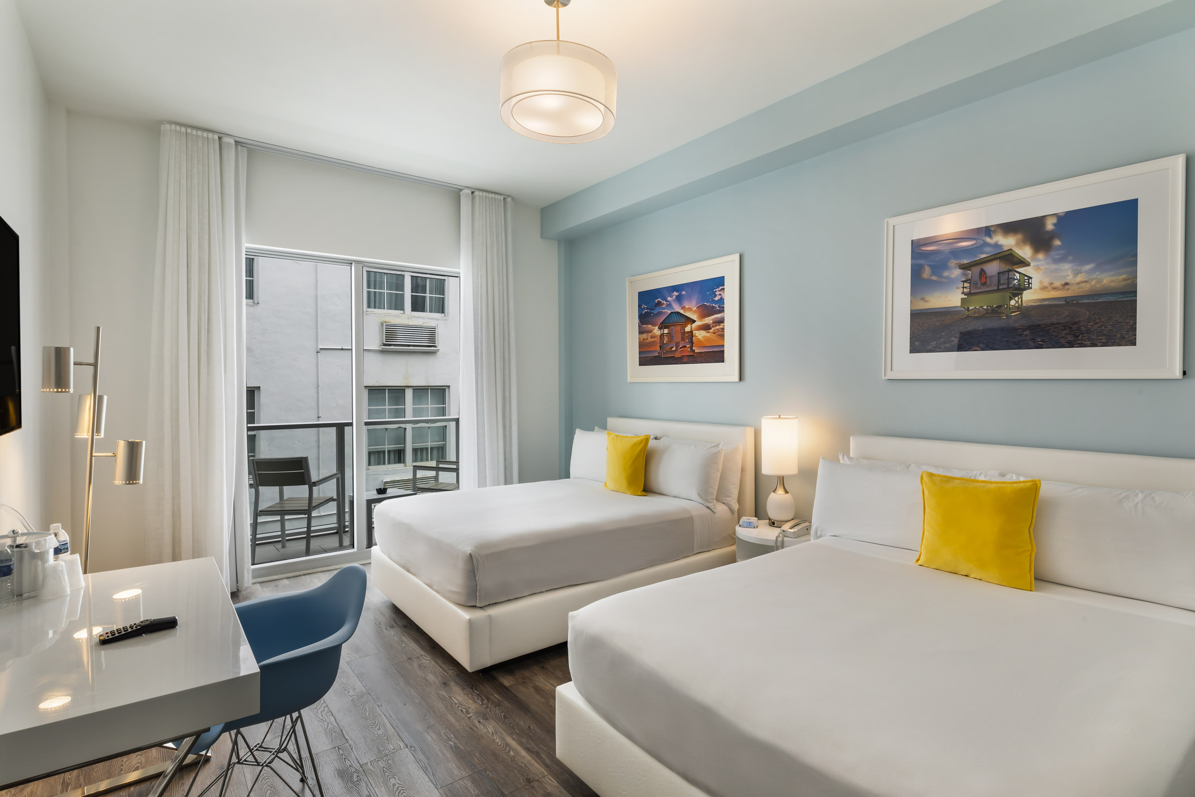 A hotel room with two beds, a desk, and a balcony