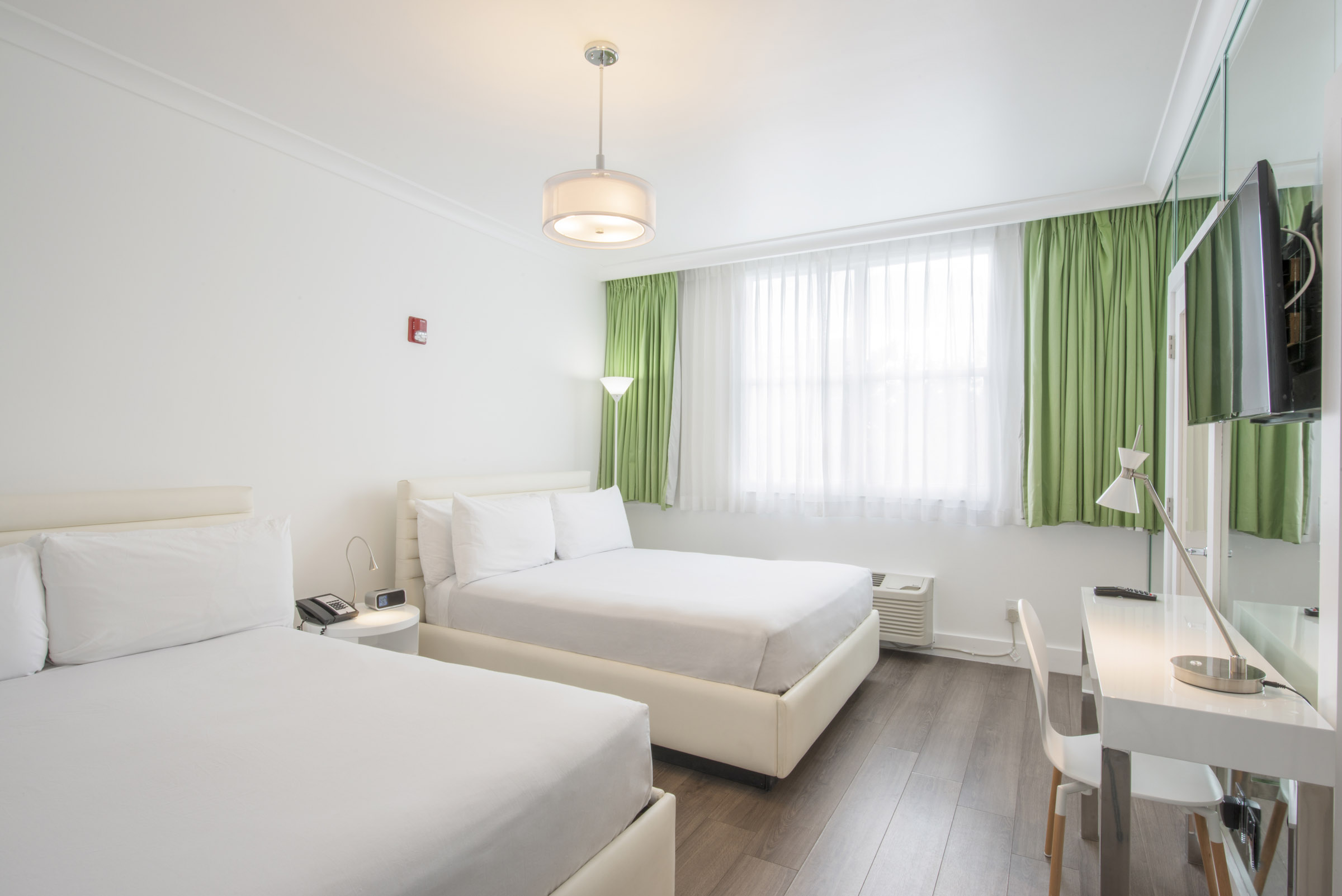 A clean and modern hotel room with two beds, a desk, and a window.