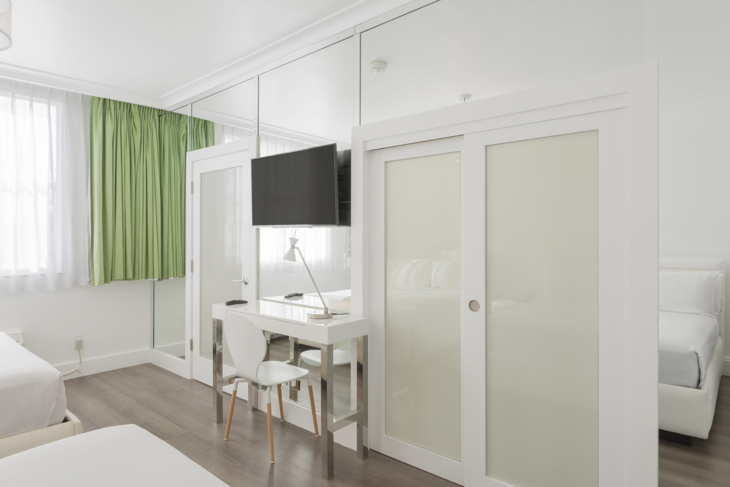 A bright and clean guest room with a desk, TV, closet, and bed.