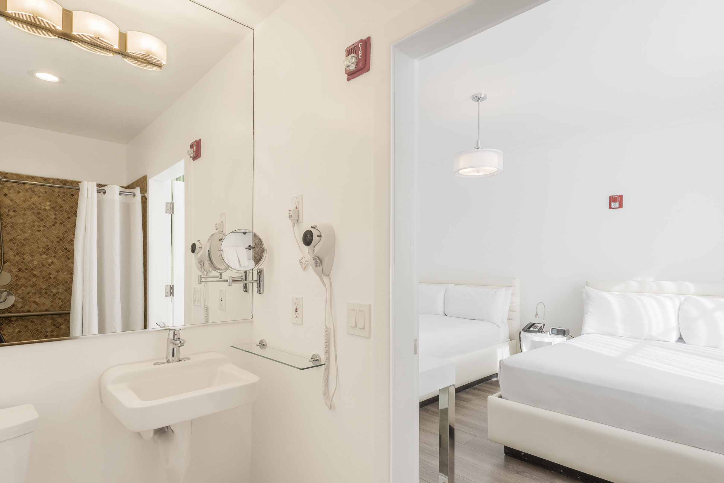 A white hotel room with a bathroom and bed