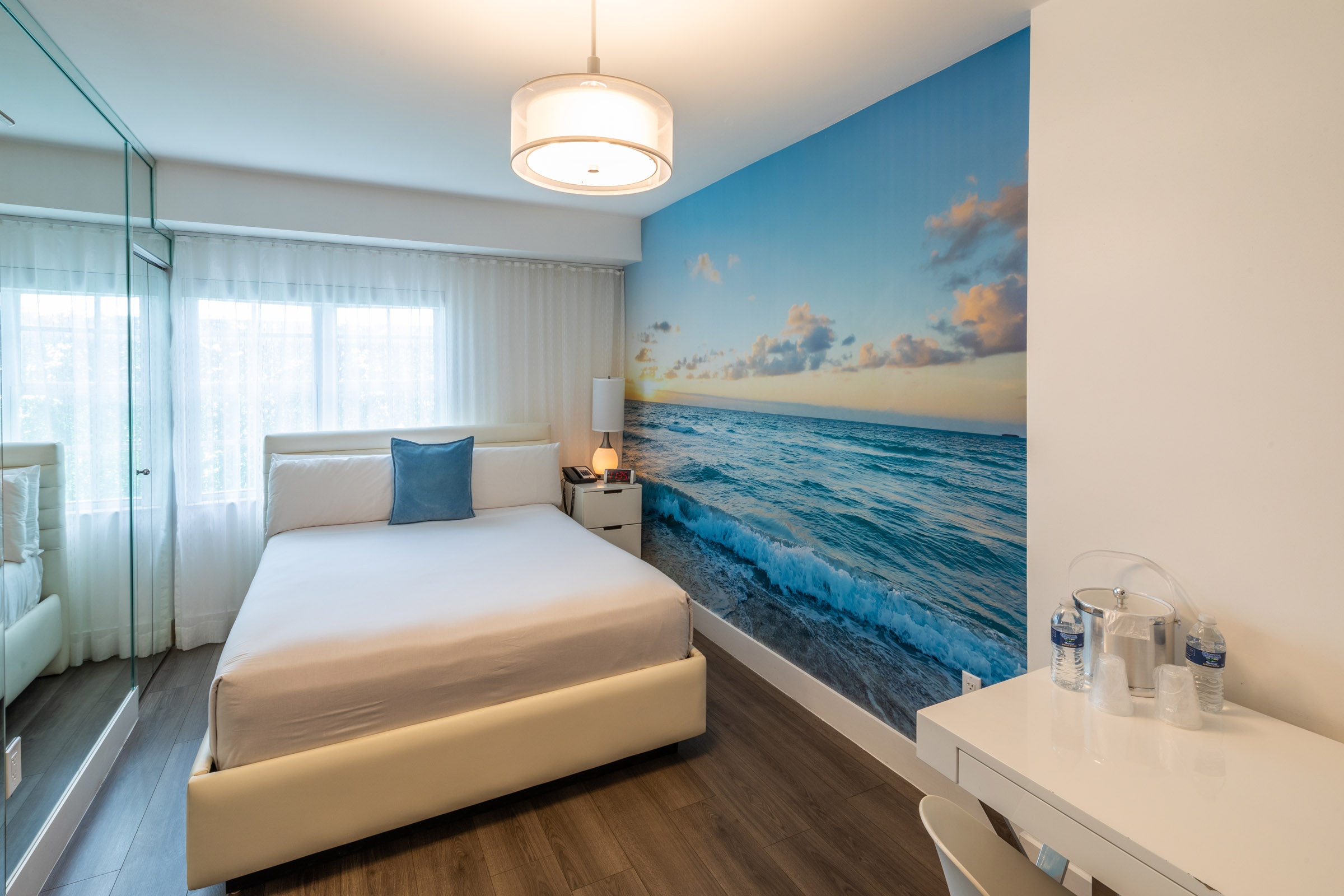 A hotel room with a large bed, a desk, and a mirror, featuring a beach-themed wall mural.