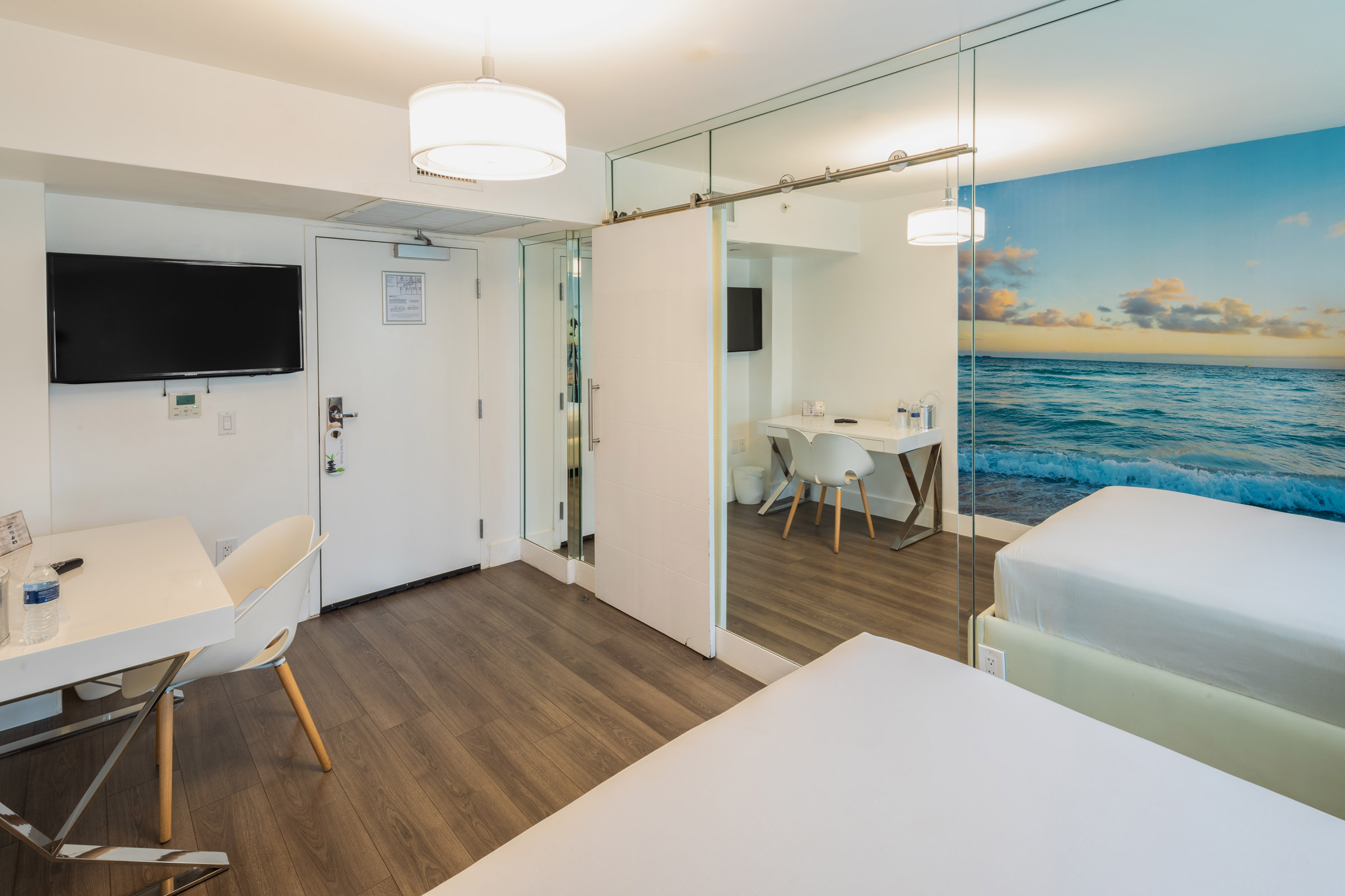 A hotel room with a desk, chair, bed, and TV on the wall.