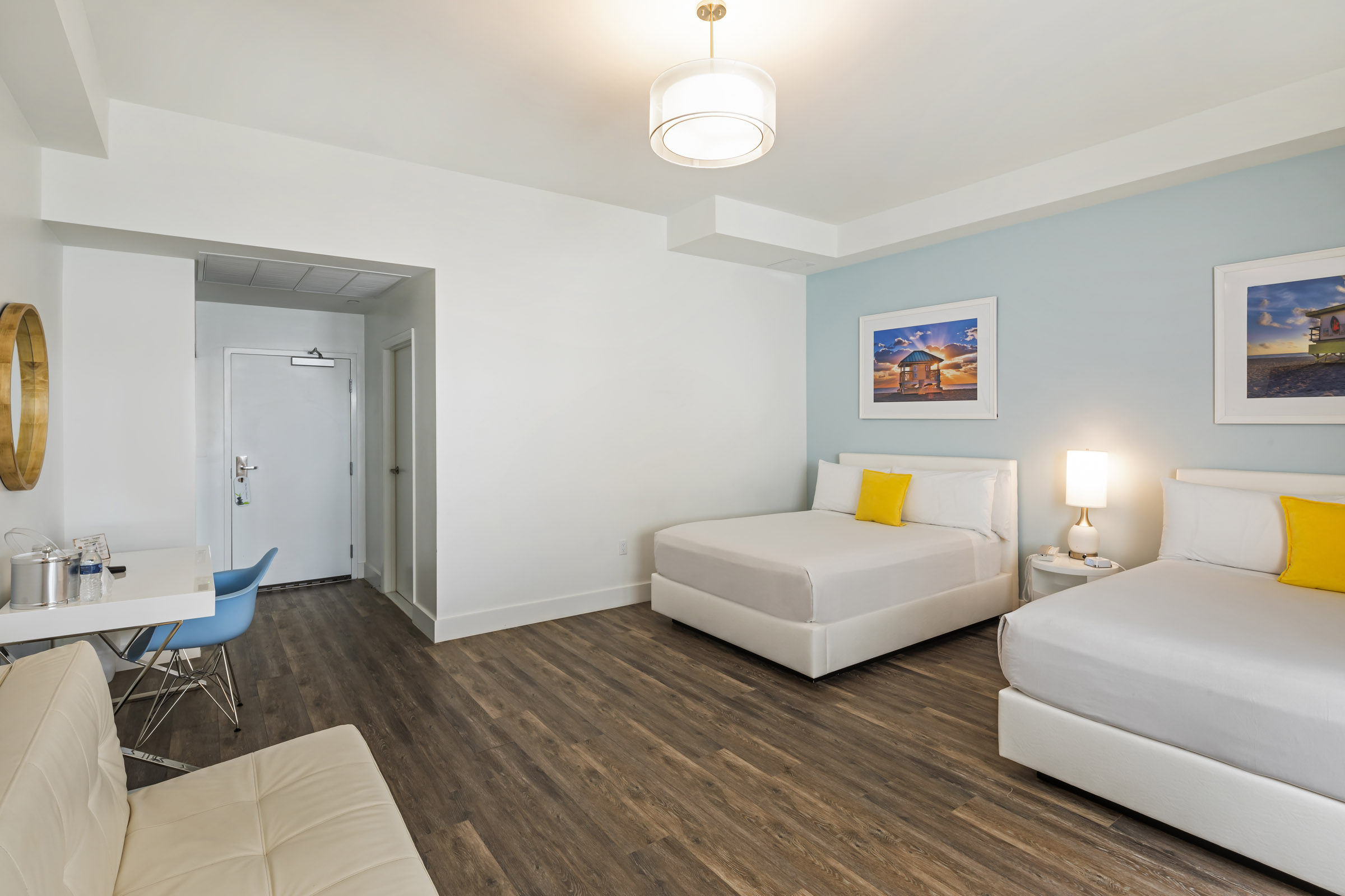 A hotel room with two beds, a sofa, a desk, and artwork on the walls.