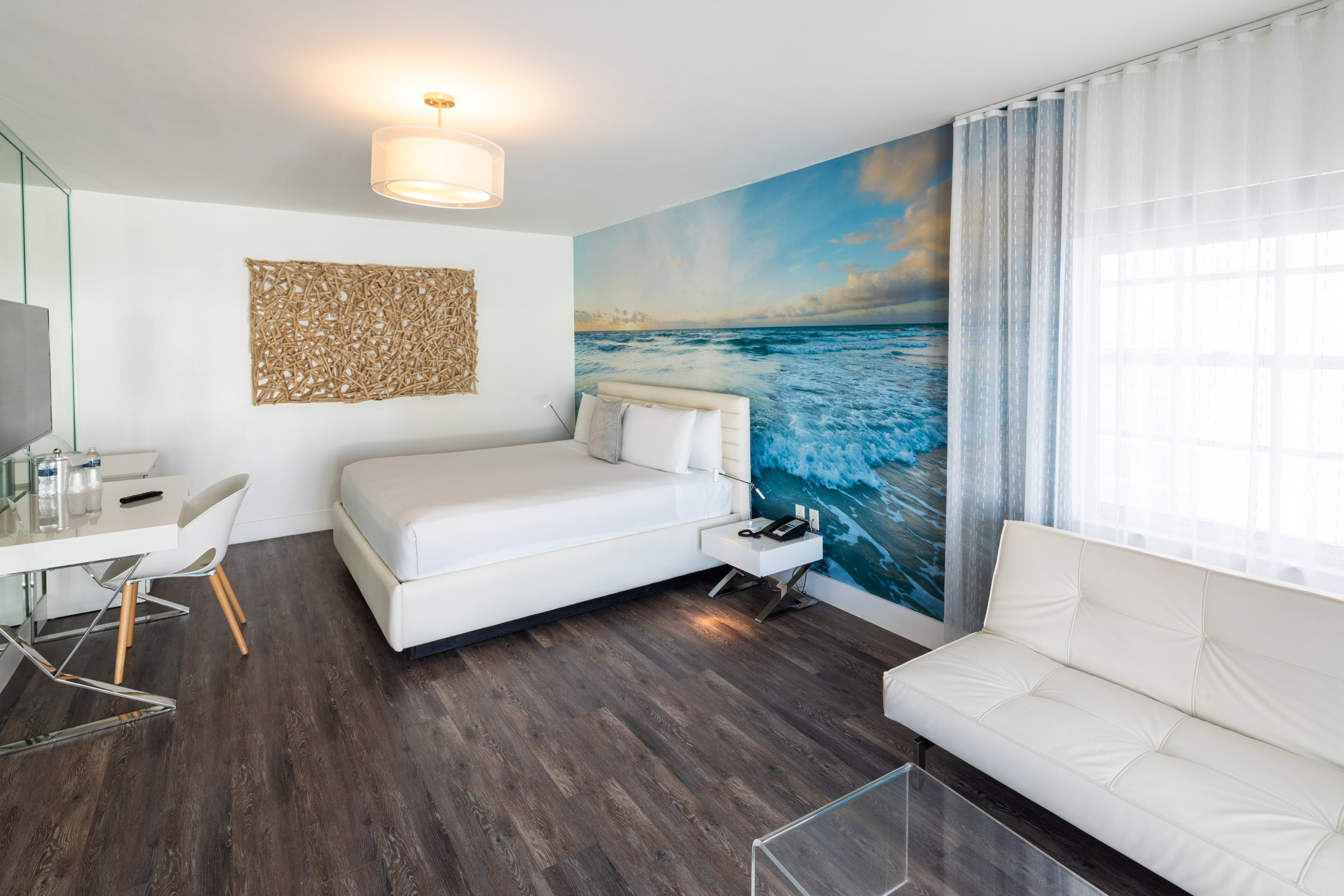 A hotel room with a bed, sofa, desk, and ocean mural