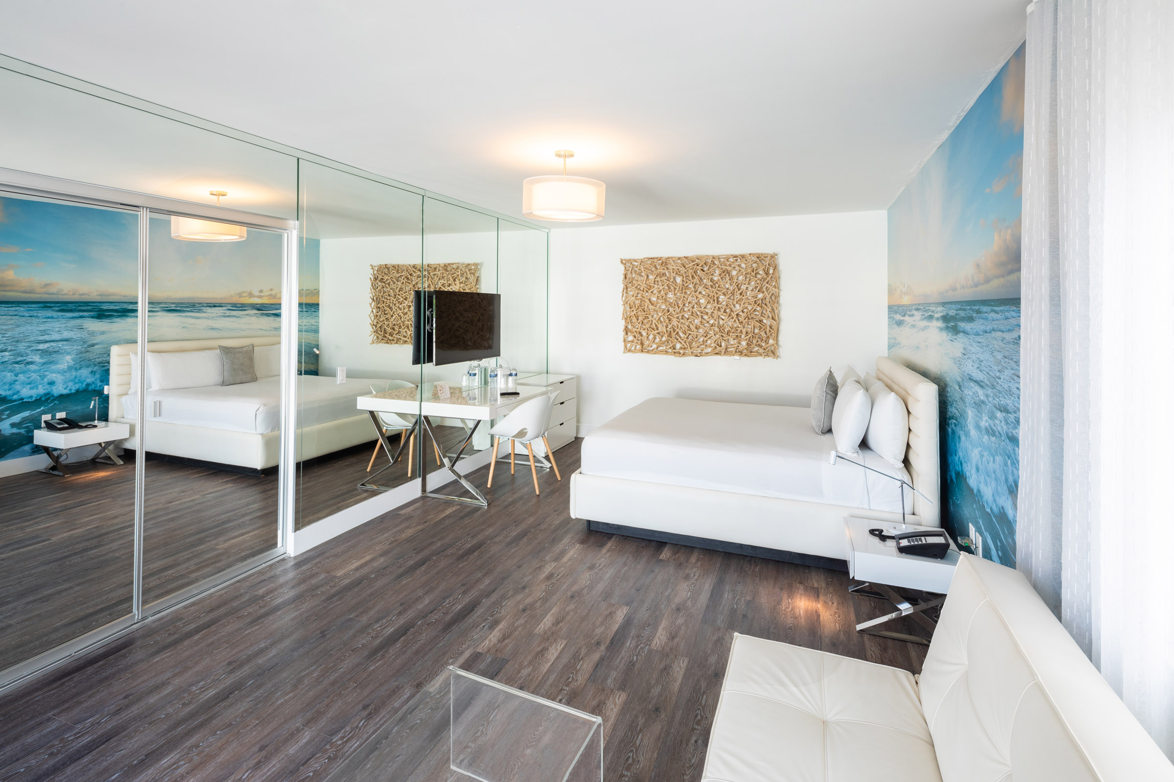 A modern hotel suite with a large bed, sofa, desk, and ocean view artwork