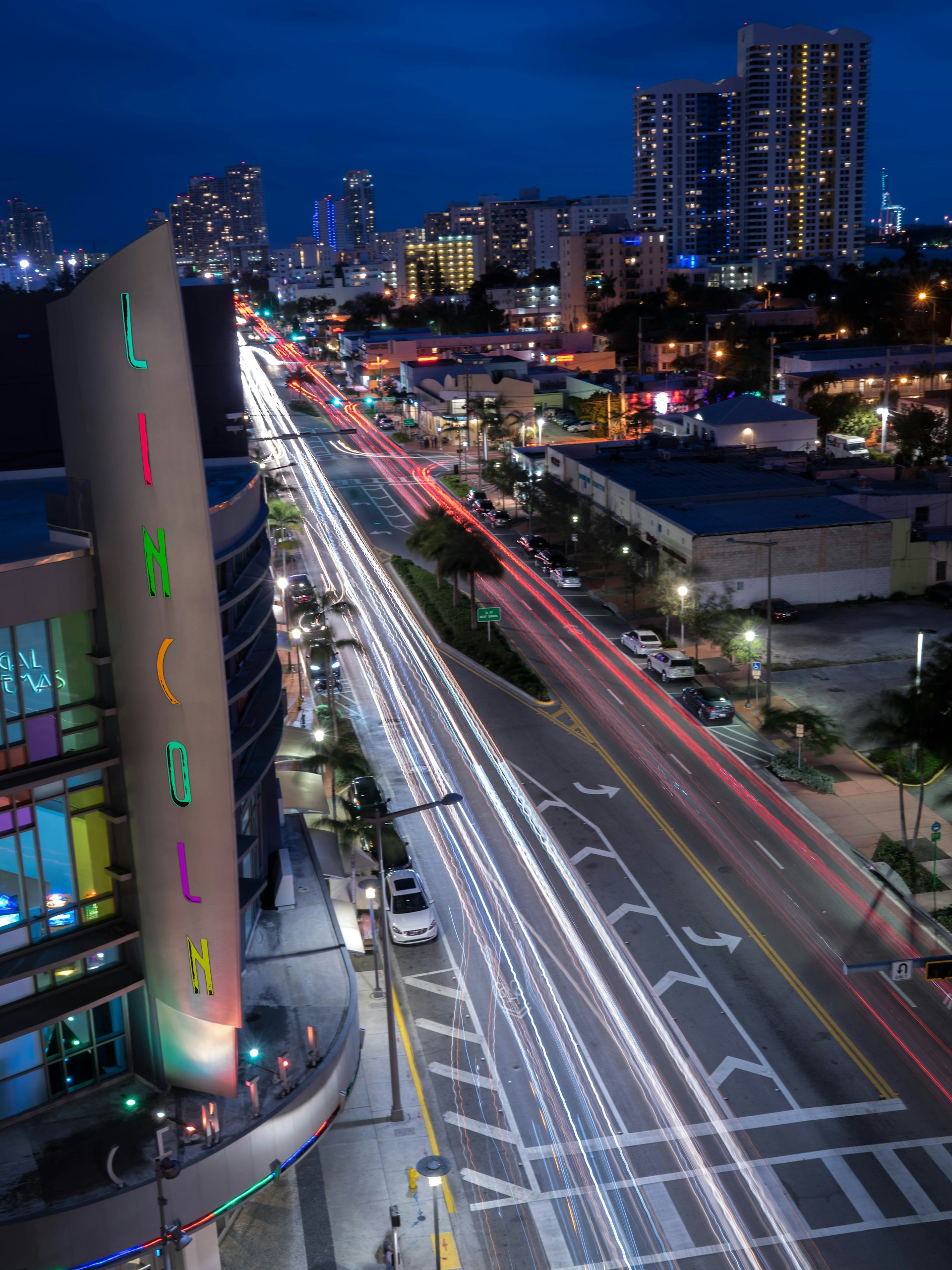 A nighttime view of a building with neon signs on the side, with a city street and traffic in the background.